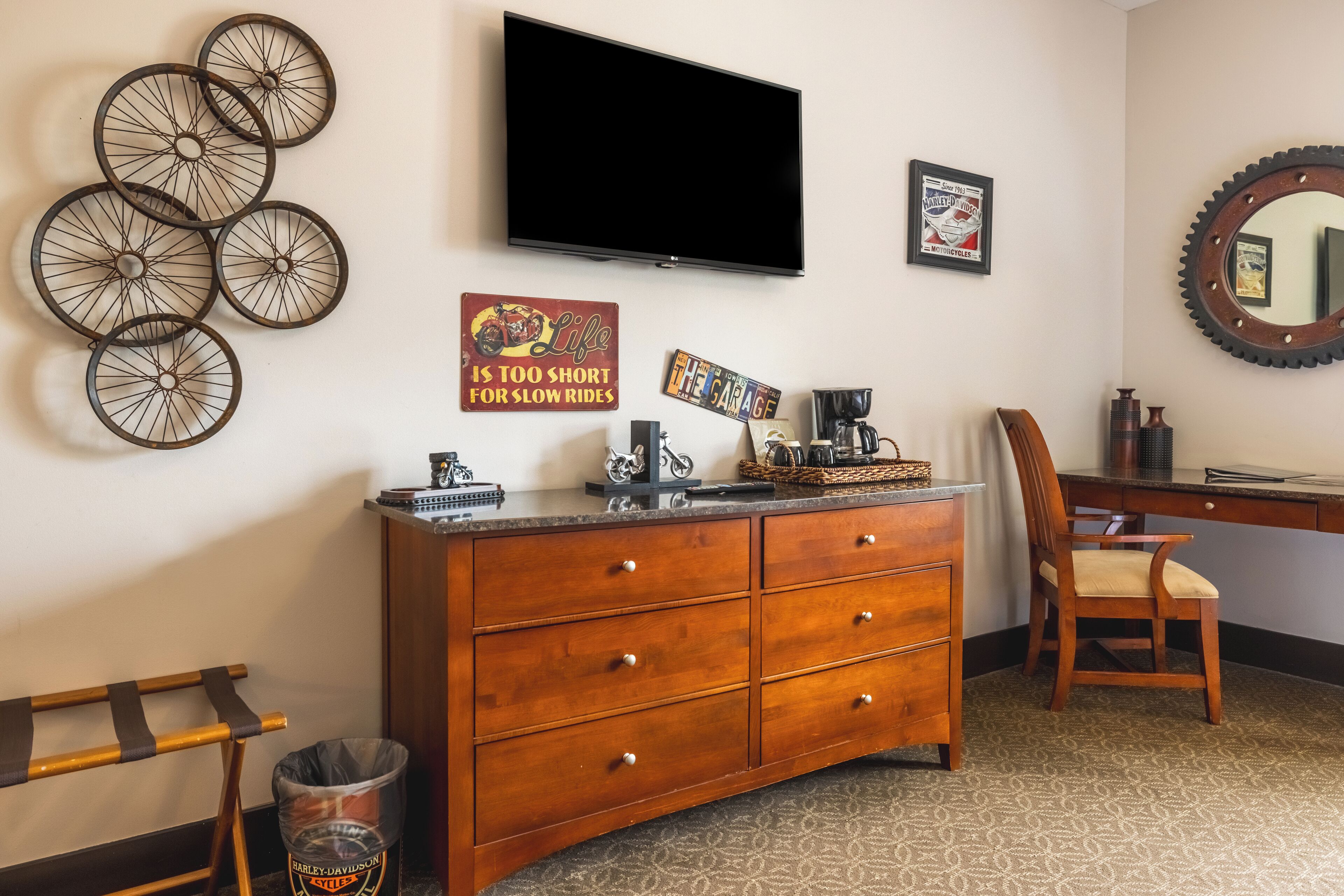 A room with a wooden dresser, a television mounted on the wall, and a motorcycle-themed sign.