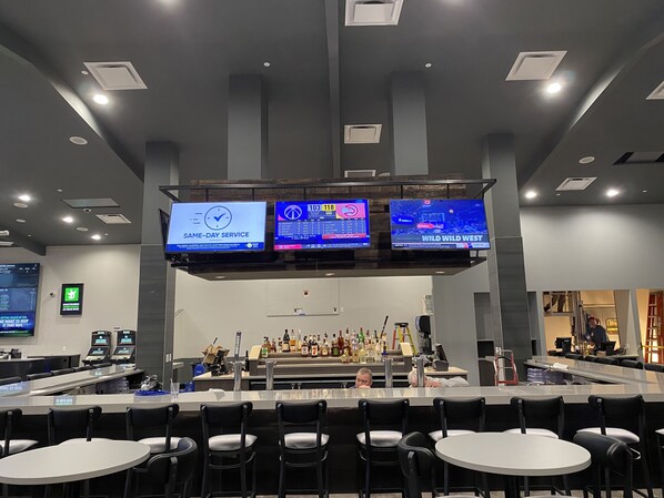 A bar area with multiple screens displaying sports content, a bar counter with various bottles, and seating arrangements.