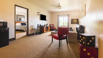Habitación de hotel con alfombra estampada, una silla roja, televisión, ventilador de techo y una ventana con cortinas.