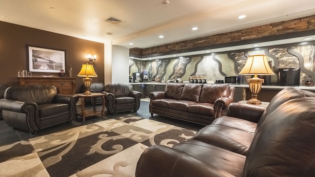 Un vaste espace de vie agrémenté de canapés en cuir, d’un tapis à motifs et d’un coin bar avec un mur arrière en pierre.