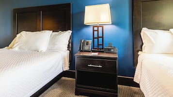 A hotel room with two beds, a nightstand with a lamp, a phone, and a drawer.