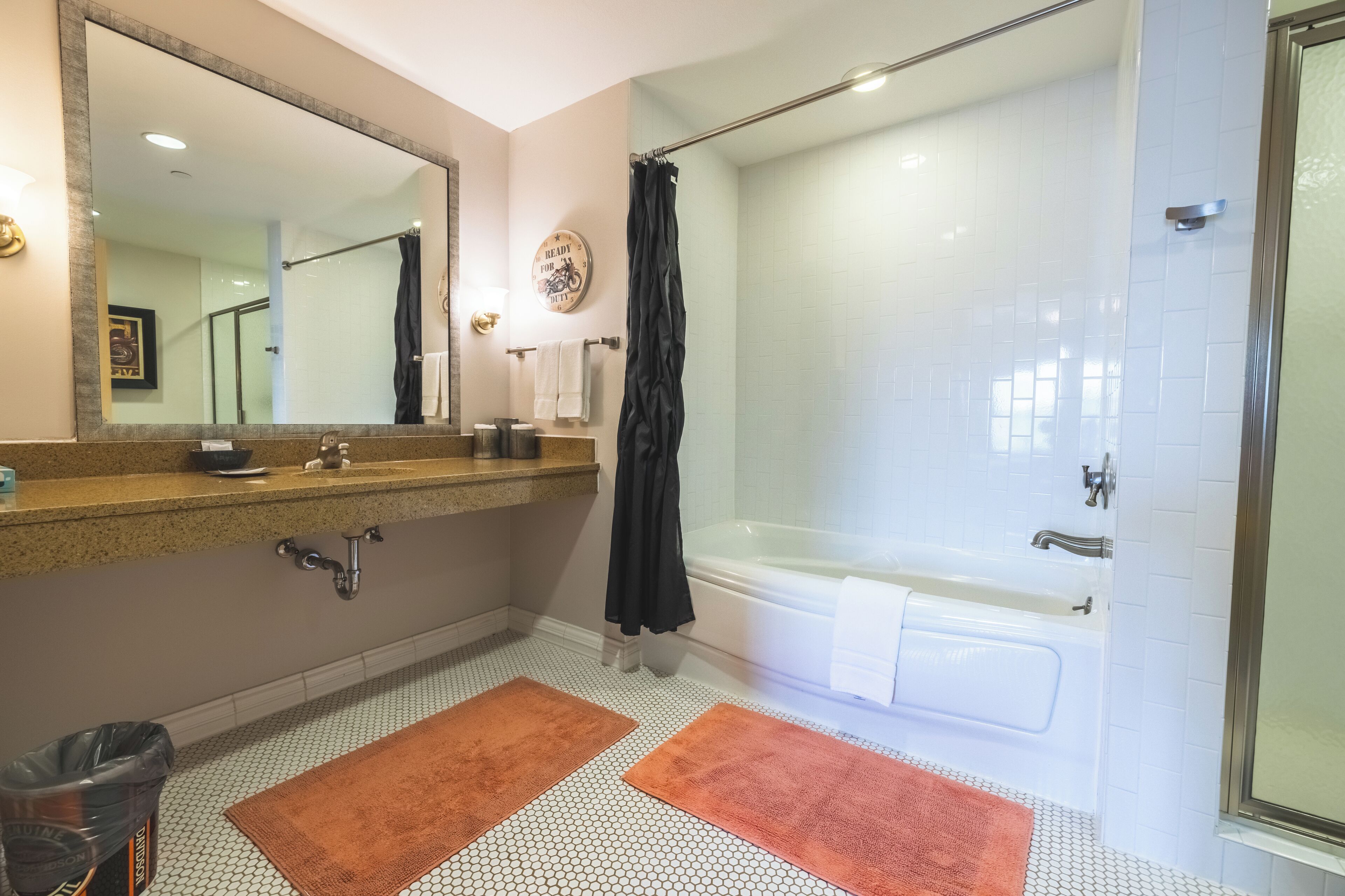 A bathroom with a large mirror, a bathtub, and two towels on the floor.