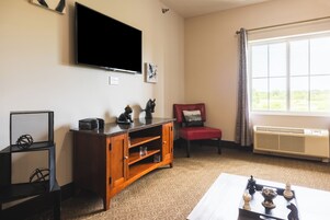 Una sala de estar con un televisor de pantalla plana, un mueble de madera para entretenimiento, un sillón rojo y un ventanal con vistas a la vegetación.
