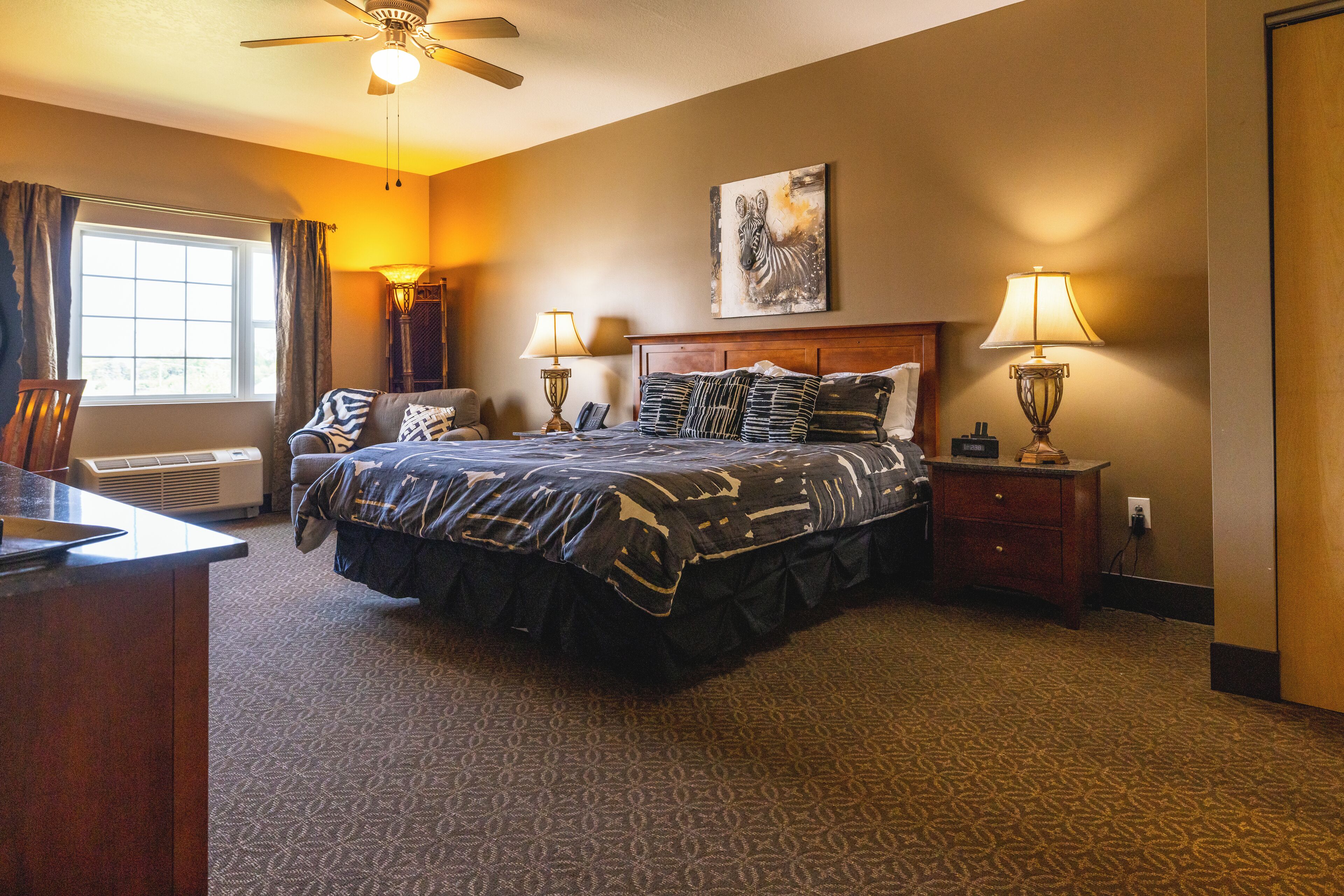 A hotel room with a large bed, two bedside lamps, a ceiling fan, and a window with curtains.