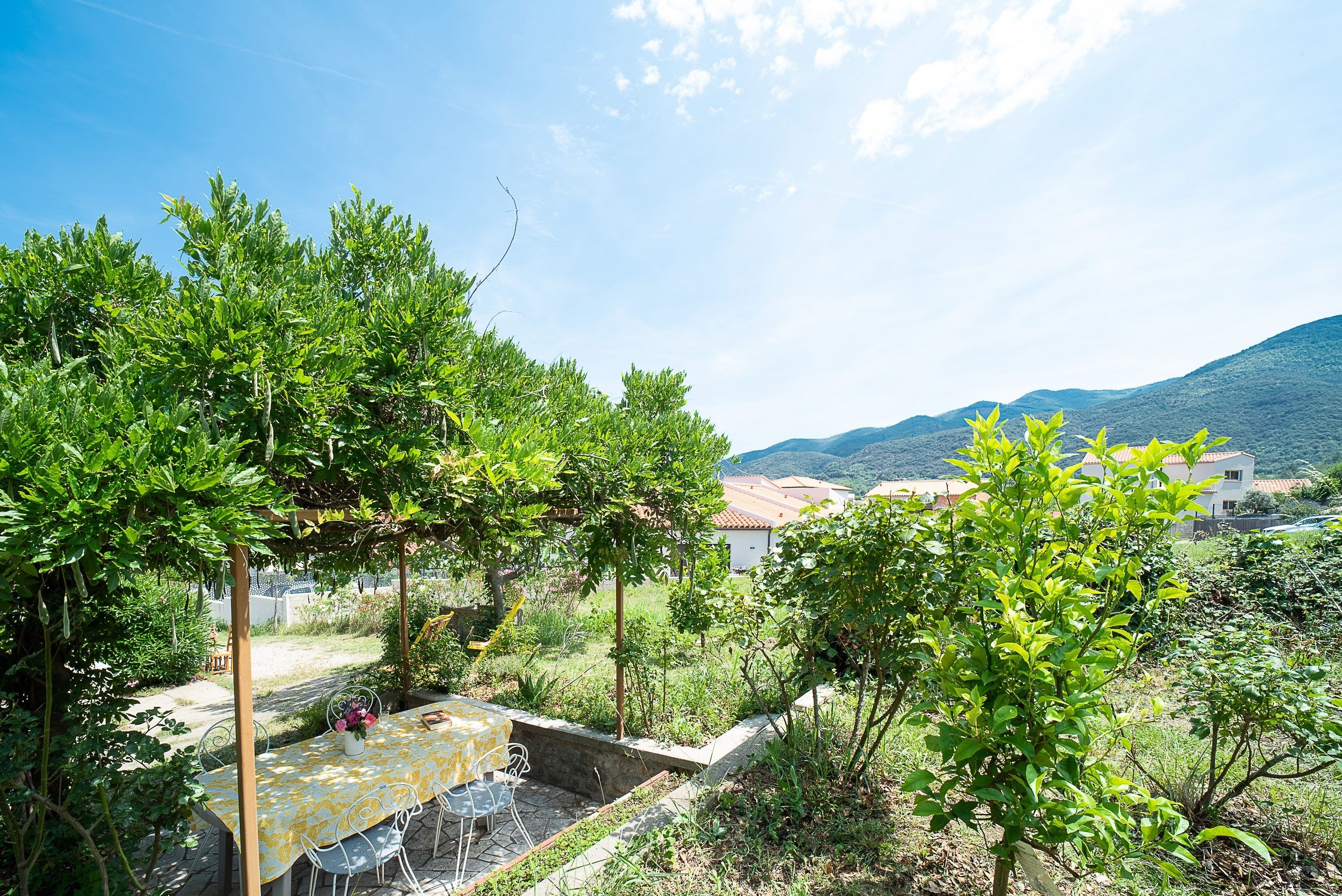 A patio with a table and chairs, surrounded by greenery and a view of distant buildings and hills.