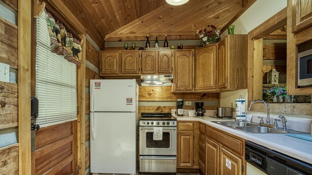 A kitchen with wooden cabinets, a refrigerator, an oven, a sink, and a dishwasher. - Lover's Hideaway #1616 (Sevierville)