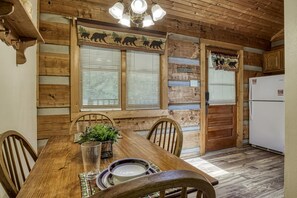 A wooden dining table with chairs, a plant, and a window with blinds. - Lover's Hideaway #1616 (Sevierville)