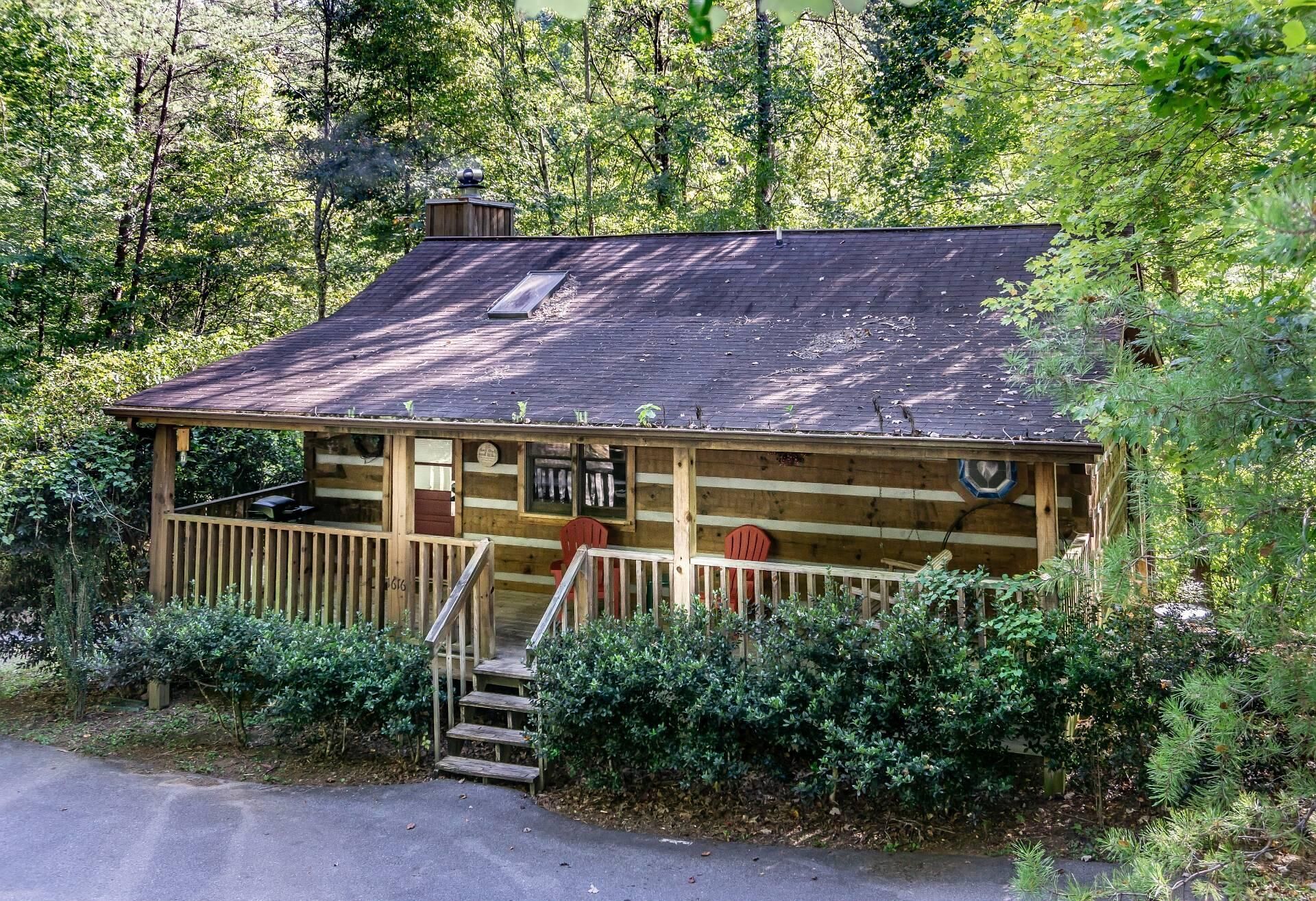 A rustic cabin with a wooden deck, a chimney, and a small porch with steps leading up to it.