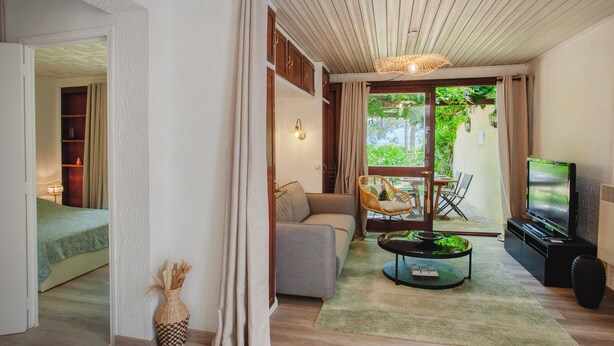 A modern living room with a sofa, coffee table, and TV. There is a balcony with a view of greenery. - Bungalow U Prato - 100m de la mer (Lumio)