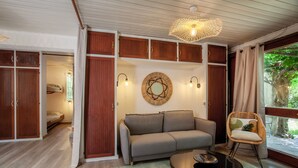 A cozy living room with a sofa, a coffee table, and a wicker chair. There is a large mirror on the wall and a ceiling light fixture. - Bungalow U Prato - 100m de la mer (Lumio)