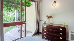 A room with a large window, a dark wooden dresser with drawers, a small vase with dried plants, and a wall-mounted light fixture. - Bungalow U Prato - 100m de la mer (Lumio)