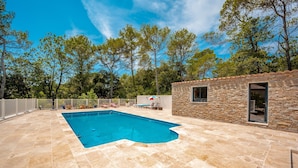 Une piscine avec une terrasse en pierre, un mur en pierre et un petit bâtiment doté d’une fenêtre.