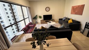 A modern living room with a sofa, TV, and a dining table with chairs. - Enjoy and Stay In Dubai Homes (Dubai)