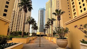 A pathway flanked by high-rise buildings, palm trees, and large planters. - Enjoy and Stay In Dubai Homes (Dubai)