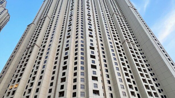 A tall, modern high-rise building with a swimming pool in the foreground. - Enjoy and Stay In Dubai Homes (Dubai)