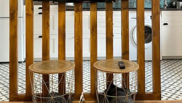 A modern kitchen with a wooden slat wall, a flat-screen TV mounted above a woven round table, and a washing machine in the background. - Apartamento Entero Para 4 Personas en Leioa. Sin Ascensor (Leioa)