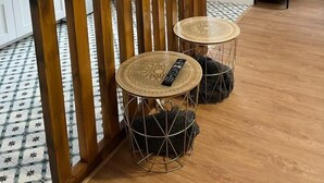A modern living room with a flat-screen TV mounted on a wooden partition, two round side tables with woven tops, and a black clock on the wall. - Apartamento Entero Para 4 Personas en Leioa. Sin Ascensor (Leioa)