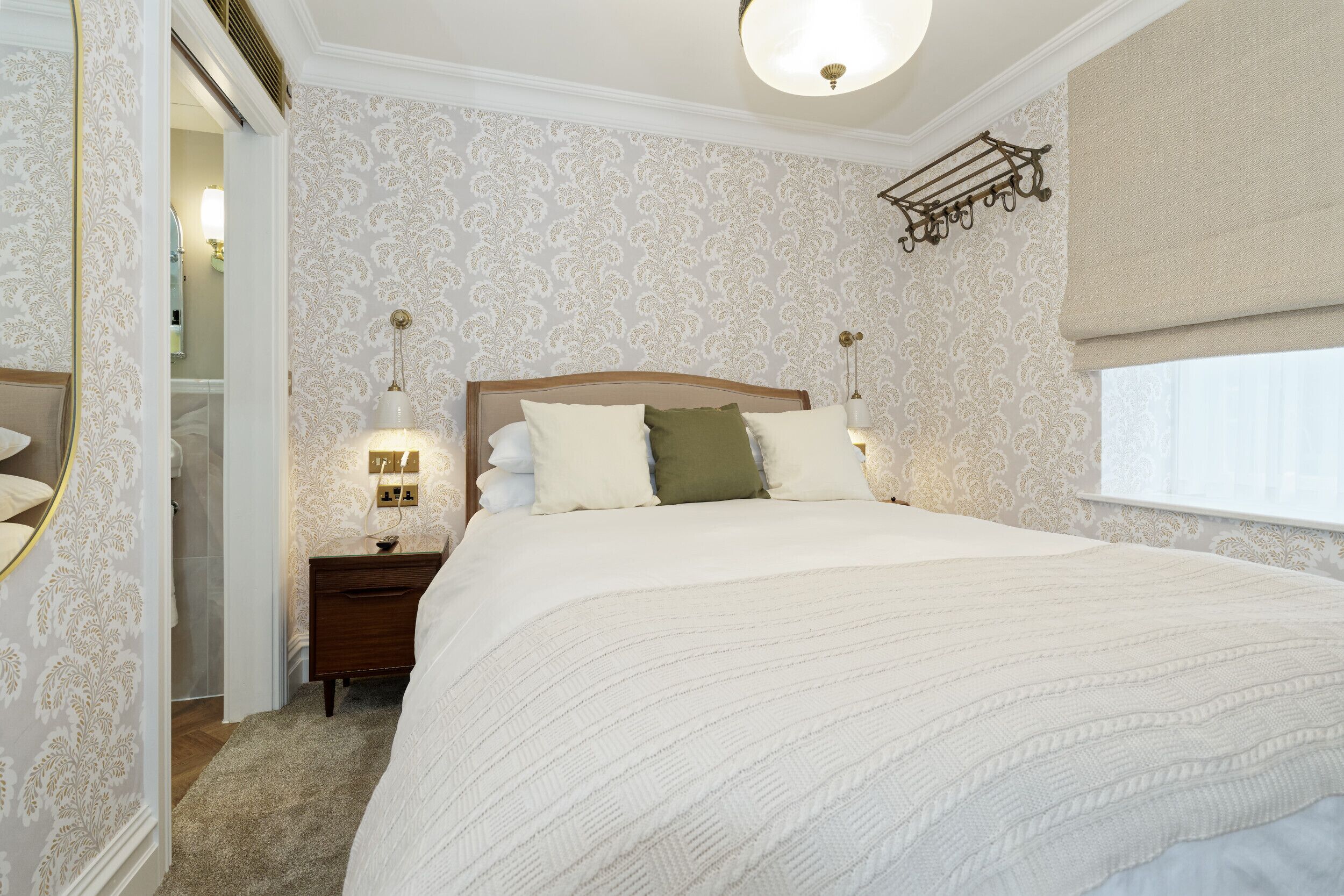 Une chambre à coucher avec un grand lit, une table de chevet, une lampe et une fenêtre avec des rideaux.