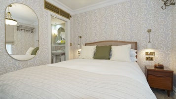 A bedroom with a large bed, a wooden nightstand, a mirror, and a wall-mounted light fixture.