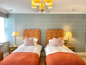 Une chambre d’hôtel avec deux lits, un lustre, un papier peint à motifs et une fenêtre avec des rideaux.