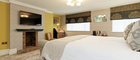 A bedroom with a fireplace, a television, a bed, and a window with a mirror.