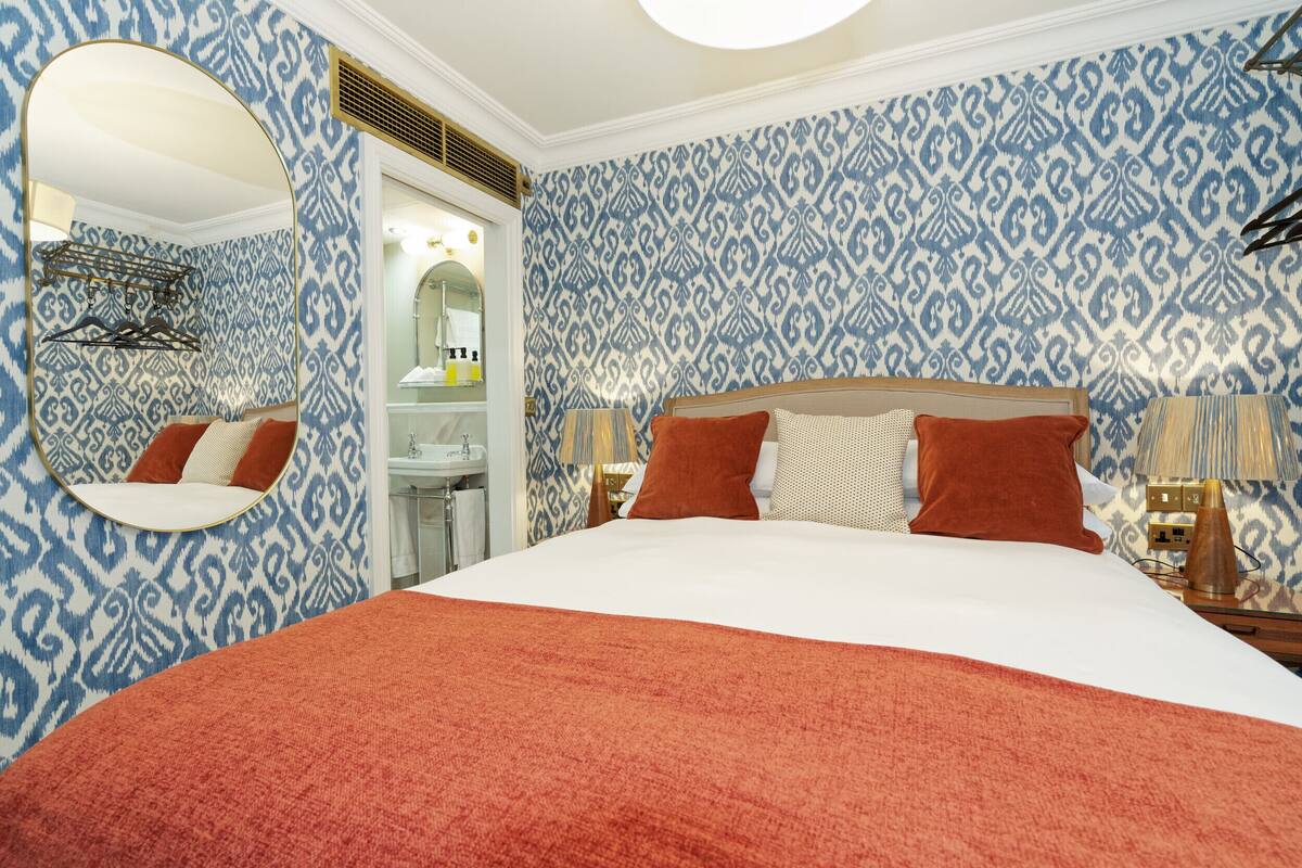A hotel room with a large bed, a mirror, a wardrobe, and patterned wallpaper.