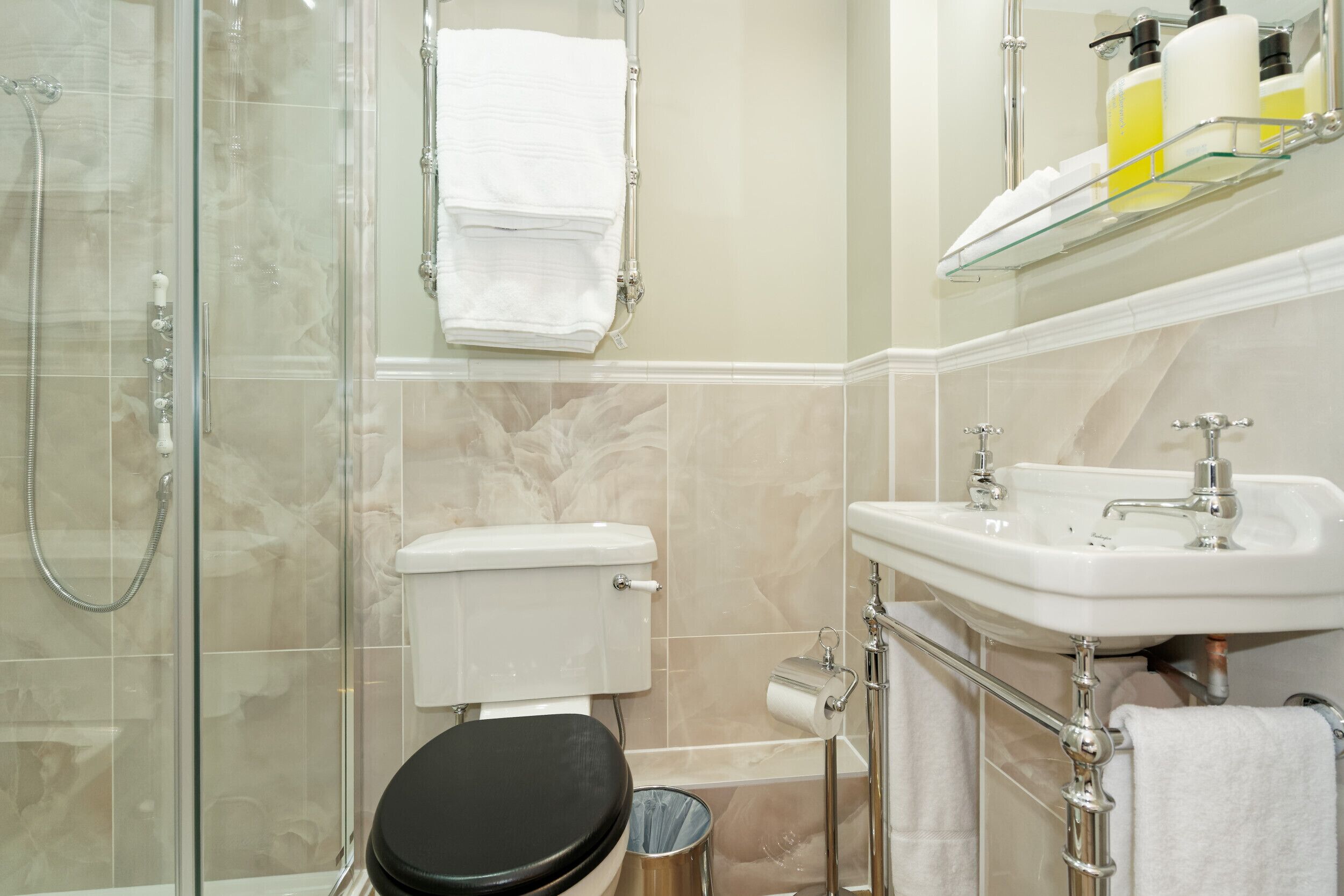 A bathroom with a glass shower enclosure, a toilet, a sink with a mirror above it, and a towel rack with towels.