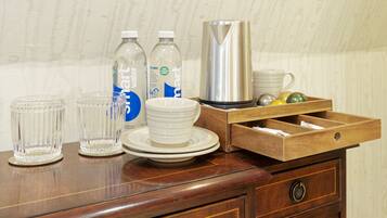 A wooden table with clear glasses, water bottles, a white mug, a stainless steel kettle, and a wooden drawer with compartments.