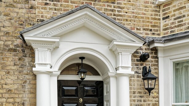 A black door with a white pediment and columns, set in a brick building.