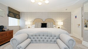 A neatly arranged bedroom with a large bed, two bedside lamps, a dresser, and a chair.