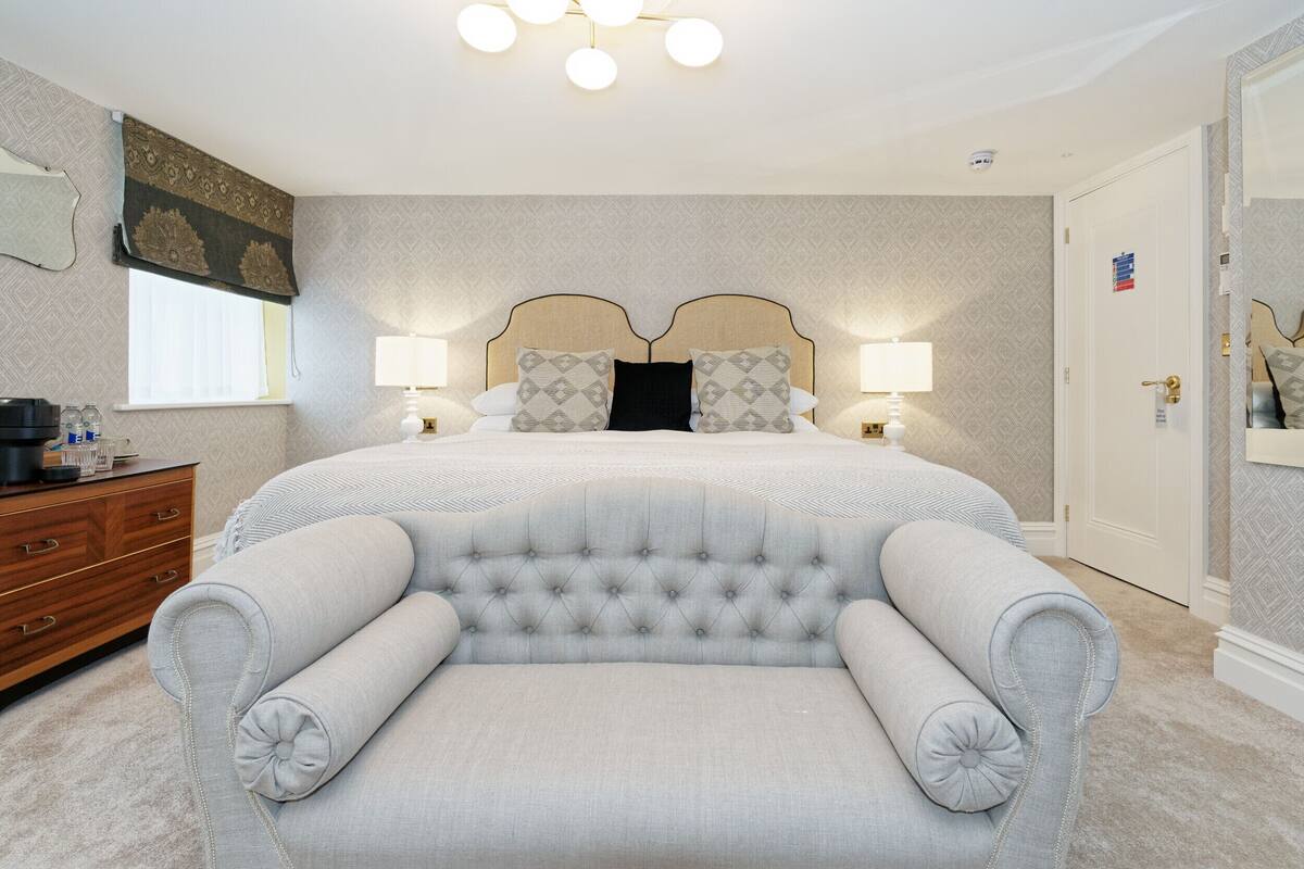 A neatly arranged bedroom with a large bed, two bedside lamps, a dresser, and a chair.