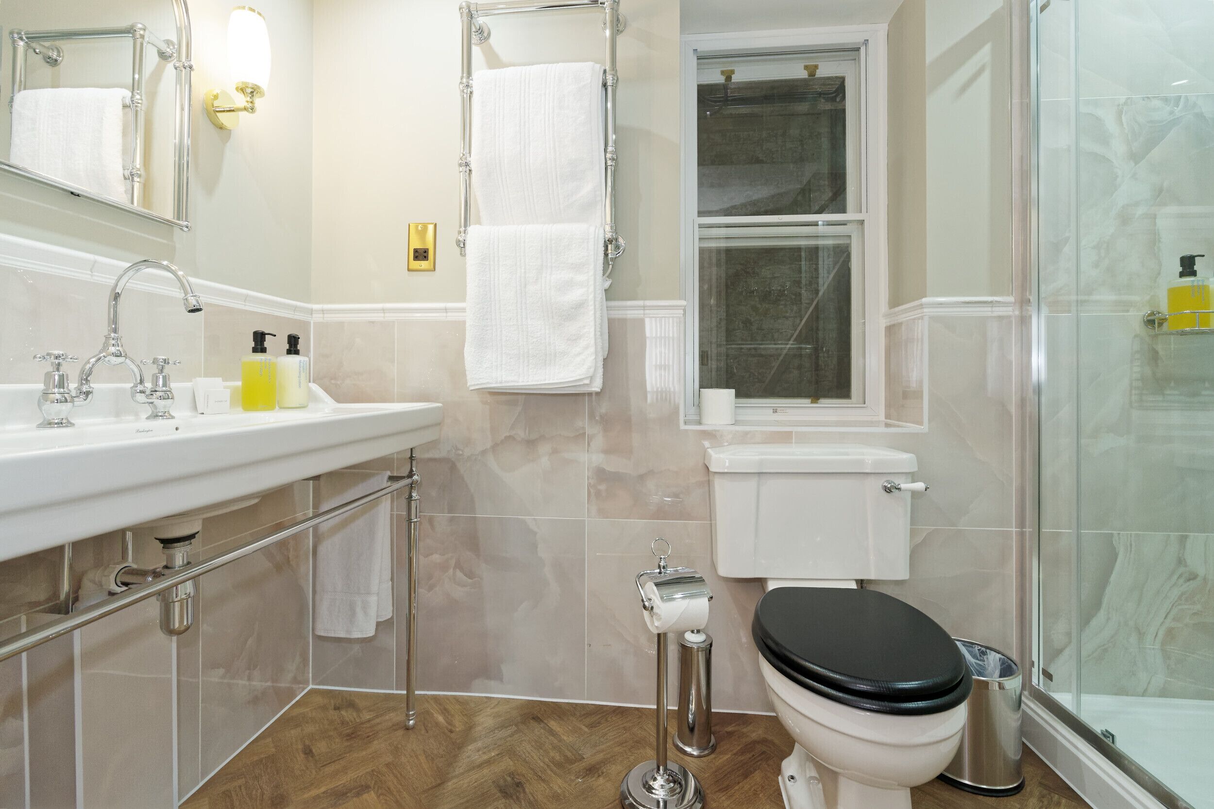 A modern bathroom with a white sink, mirror, and toilet, a glass shower enclosure, and a wooden floor.