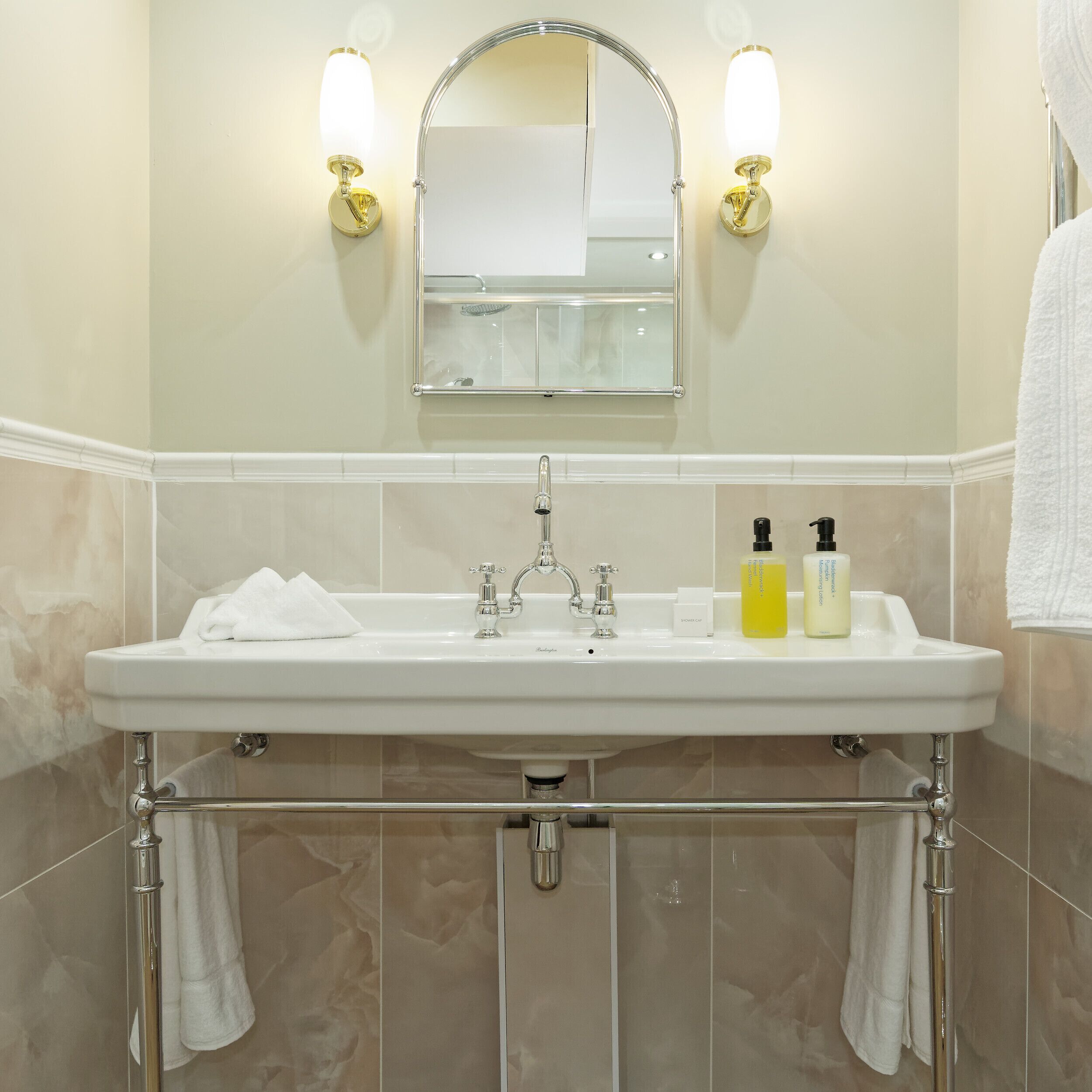 A bathroom with a white sink, two wall-mounted lights, a mirror, and a towel rack.