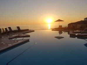 Una vista serena del atardecer sobre una piscina tranquila con sillones y sombrillas.