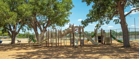 A playground with various play structures, surrounded by trees and a clear sky.
