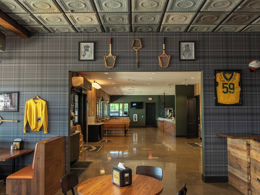 Een ruim restaurant met een hoge plafond, houten meubilair en sportmemorabilia aan de muren.