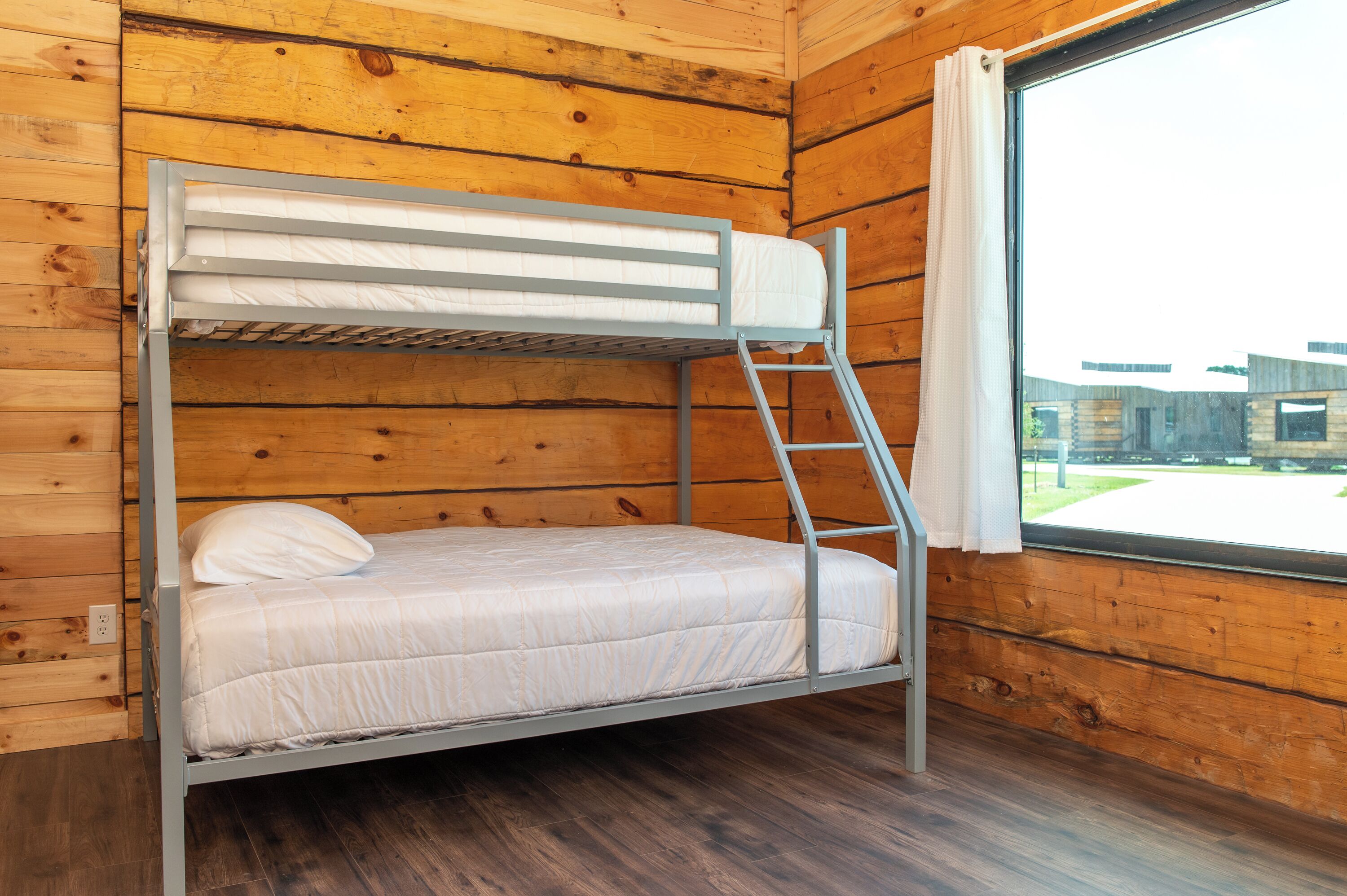 A bunk bed with a ladder, white bedding, and a window with a view of buildings.