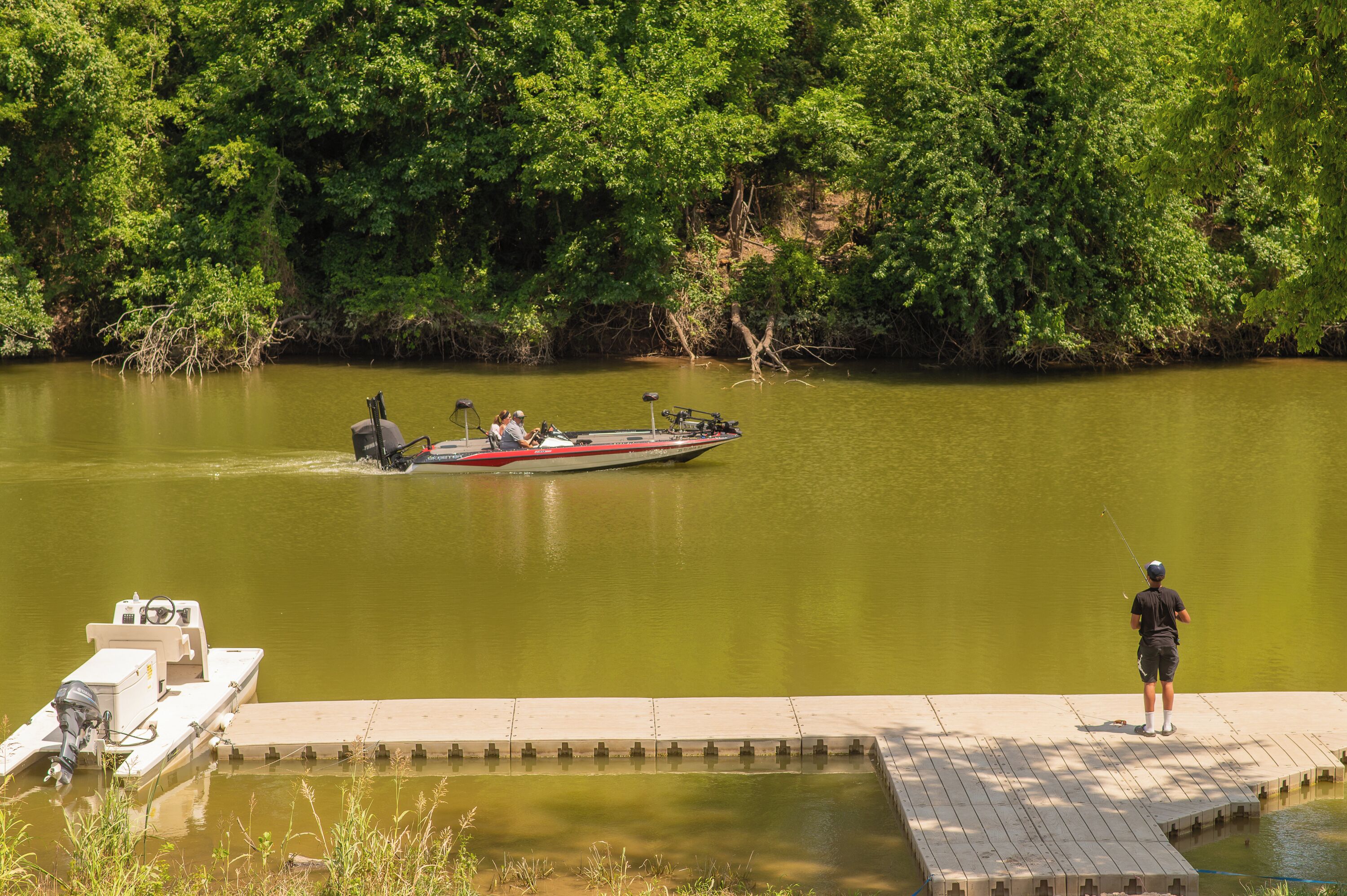 A boat docked at a wooden pier with a person fishing nearby.