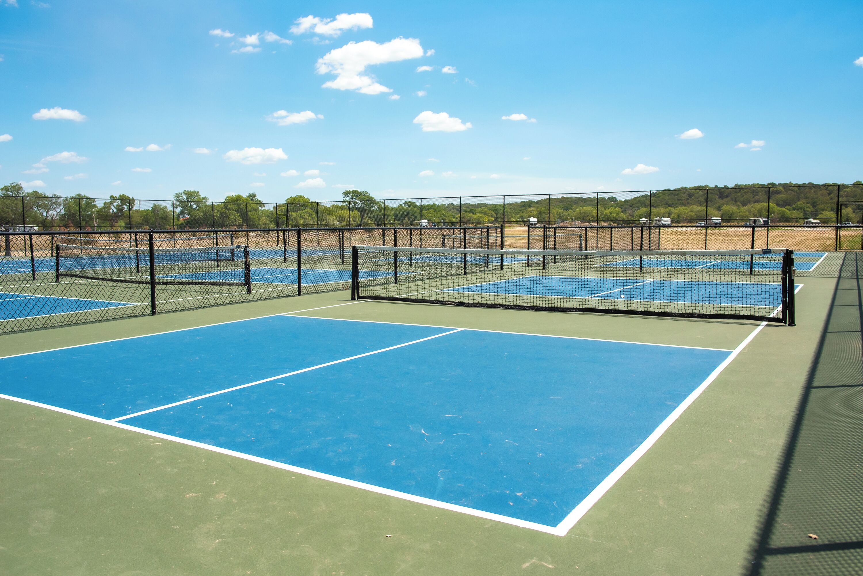 Canchas de tenis múltiples, rodeadas por una cerca, con árboles al fondo.
