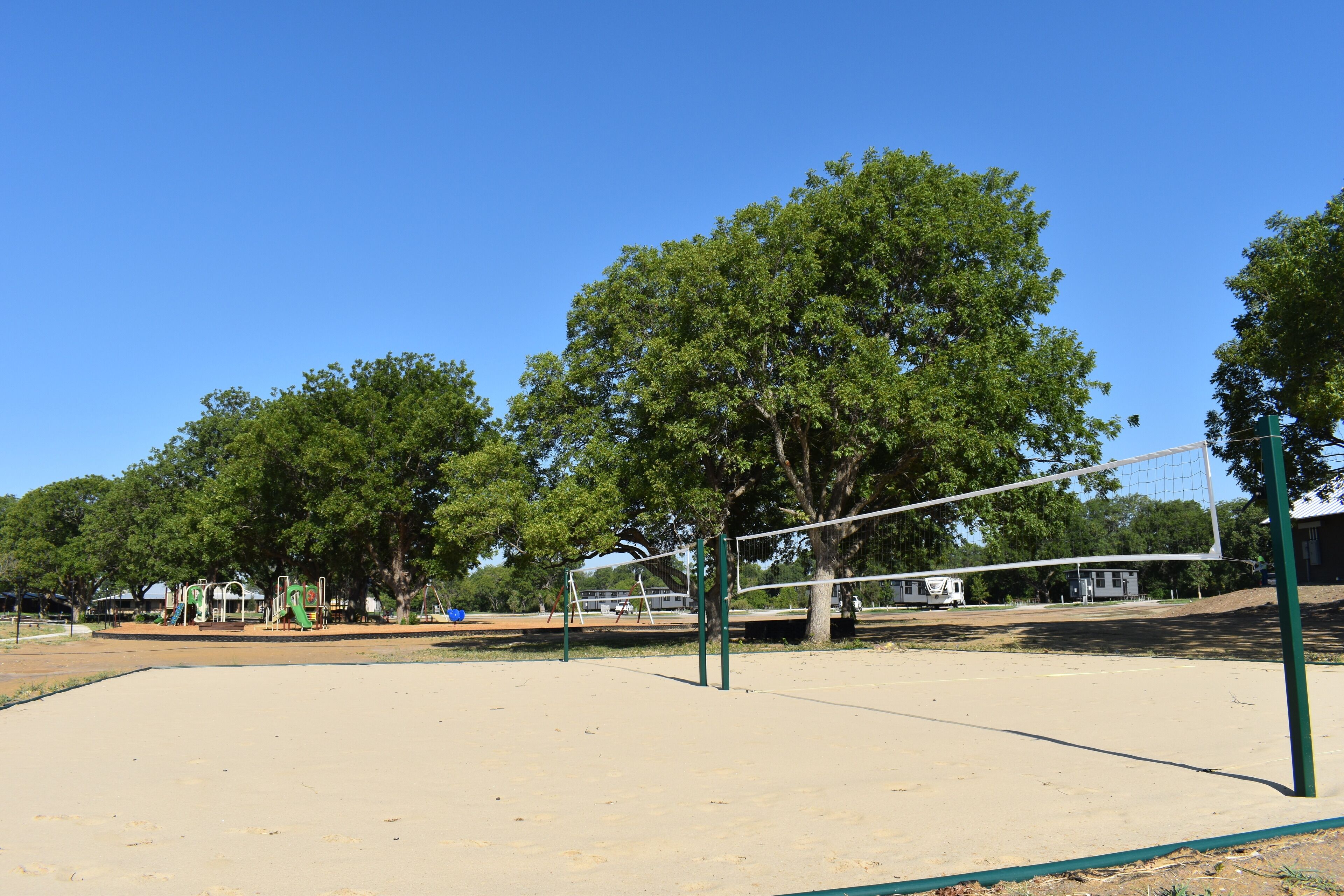 A sandy volleyball court with a net, surrounded by trees and playground equipment.