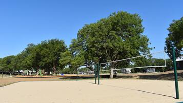 A sandy volleyball court with a net, surrounded by trees and playground equipment.