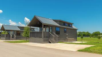 A modern two-story building with a covered porch and a small deck, situated in a grassy area with a clear sky.