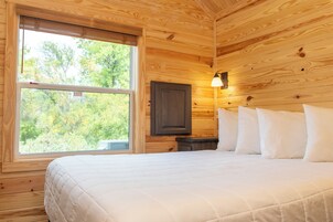 A wooden cabin room with a bed, a nightstand, a wall-mounted lamp, and a window with an 'EXIT' sign.