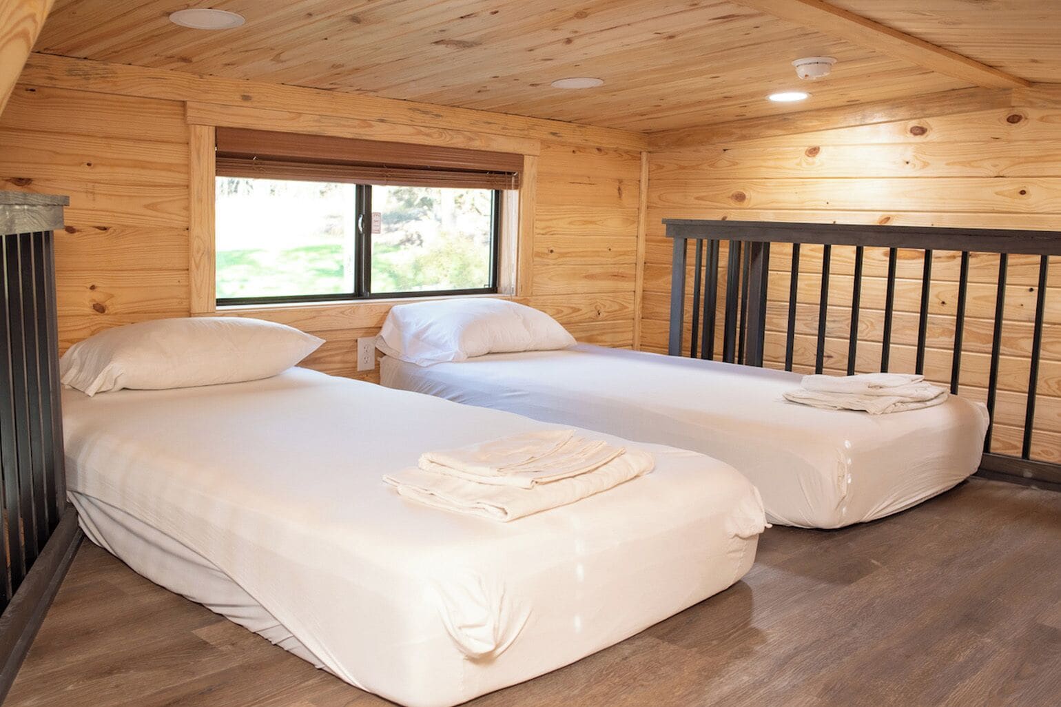 Una habitación con dos camas, paredes de madera, un ventanal e iluminación empotrada en el techo.