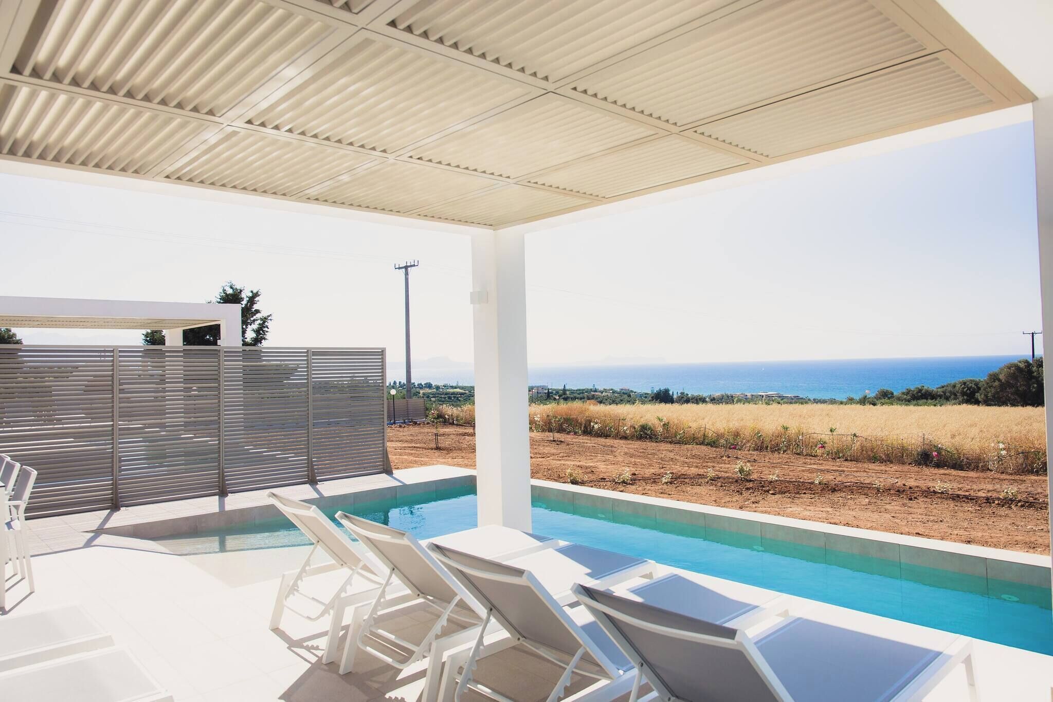 Zona de piscina con sillones de descanso, un porche cubierto y vista al mar.