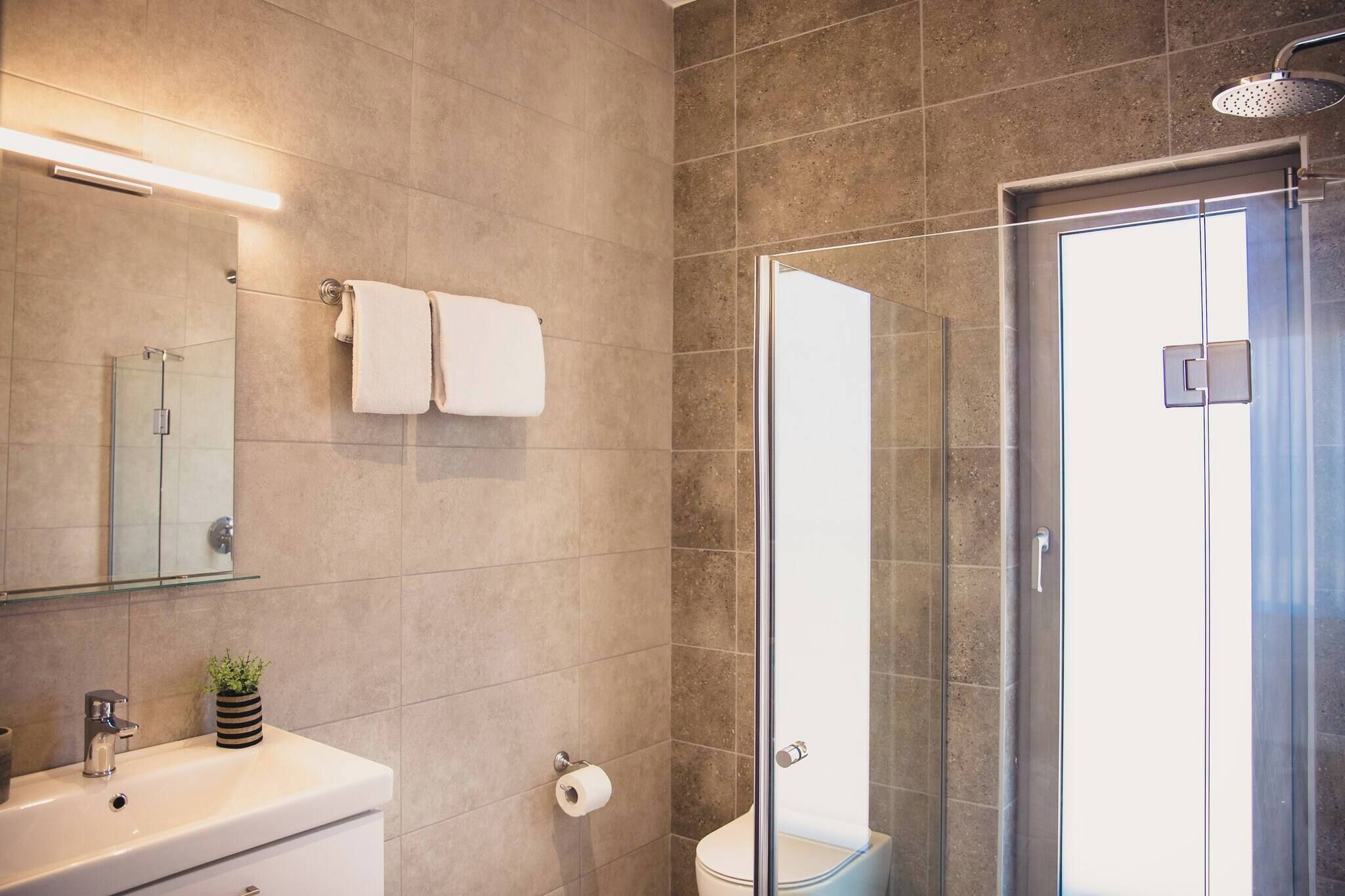 A modern bathroom with a glass shower enclosure, a toilet, and a sink with a mirror above it.