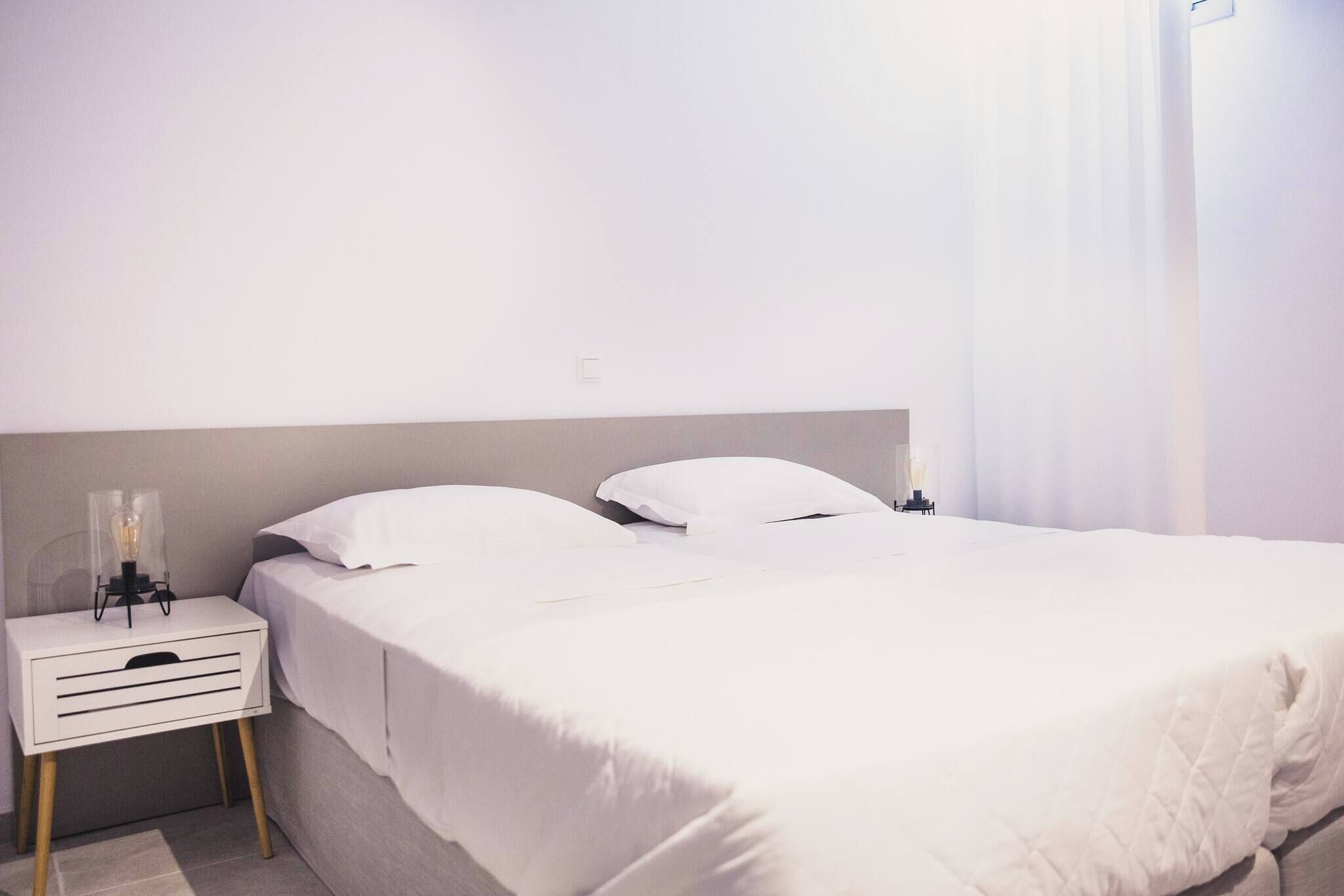 A neatly made bed with white bedding, a bedside table with a lamp, and a wall-mounted light fixture.