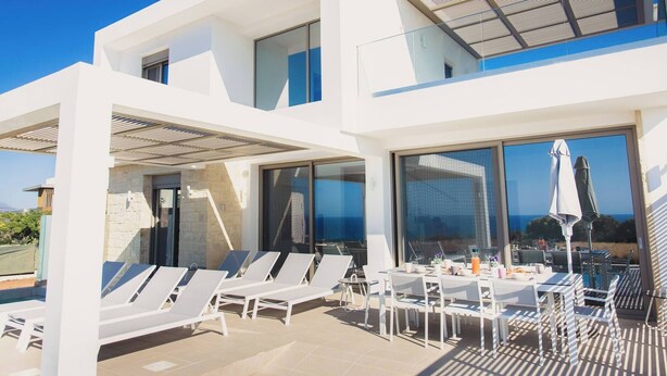 A modern building with a pool area, lounge chairs, and a dining table with umbrellas. - Starlight Villa Tropea - 4bd, 4ba, 4min To Beach (Rethymno)