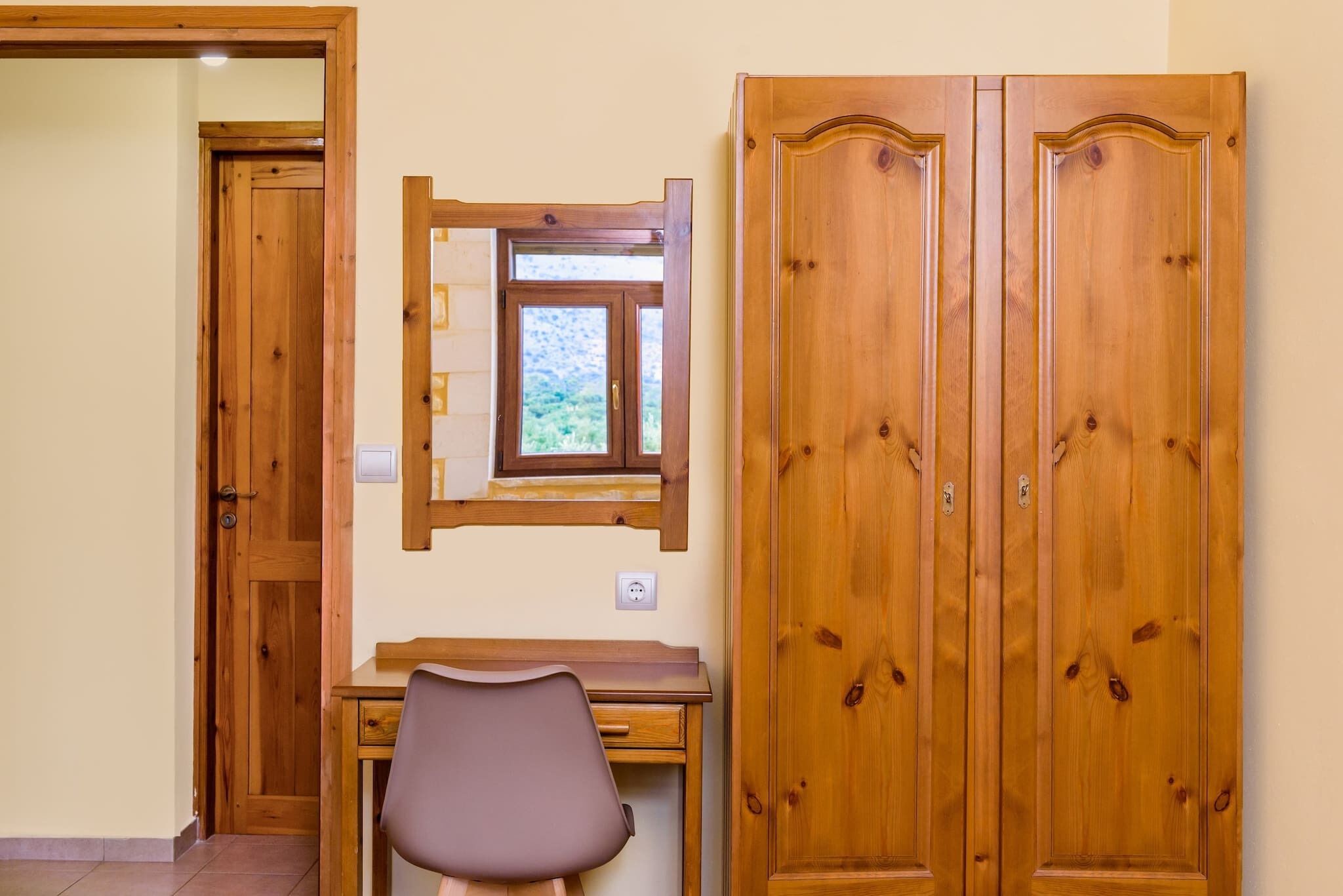A room with a desk, chair, wardrobe, and a window with a view.