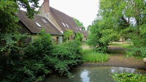 A rustic stone house with a thatched roof, surrounded by lush greenery and a small pond. - Villa Choupinière - 30 pers-Pool-1h15 Paris (Choue)
